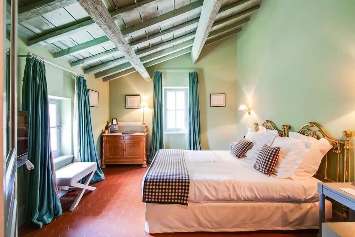 A bedroom with a large bed, wooden ceiling beams, a wooden dresser, and a bench.