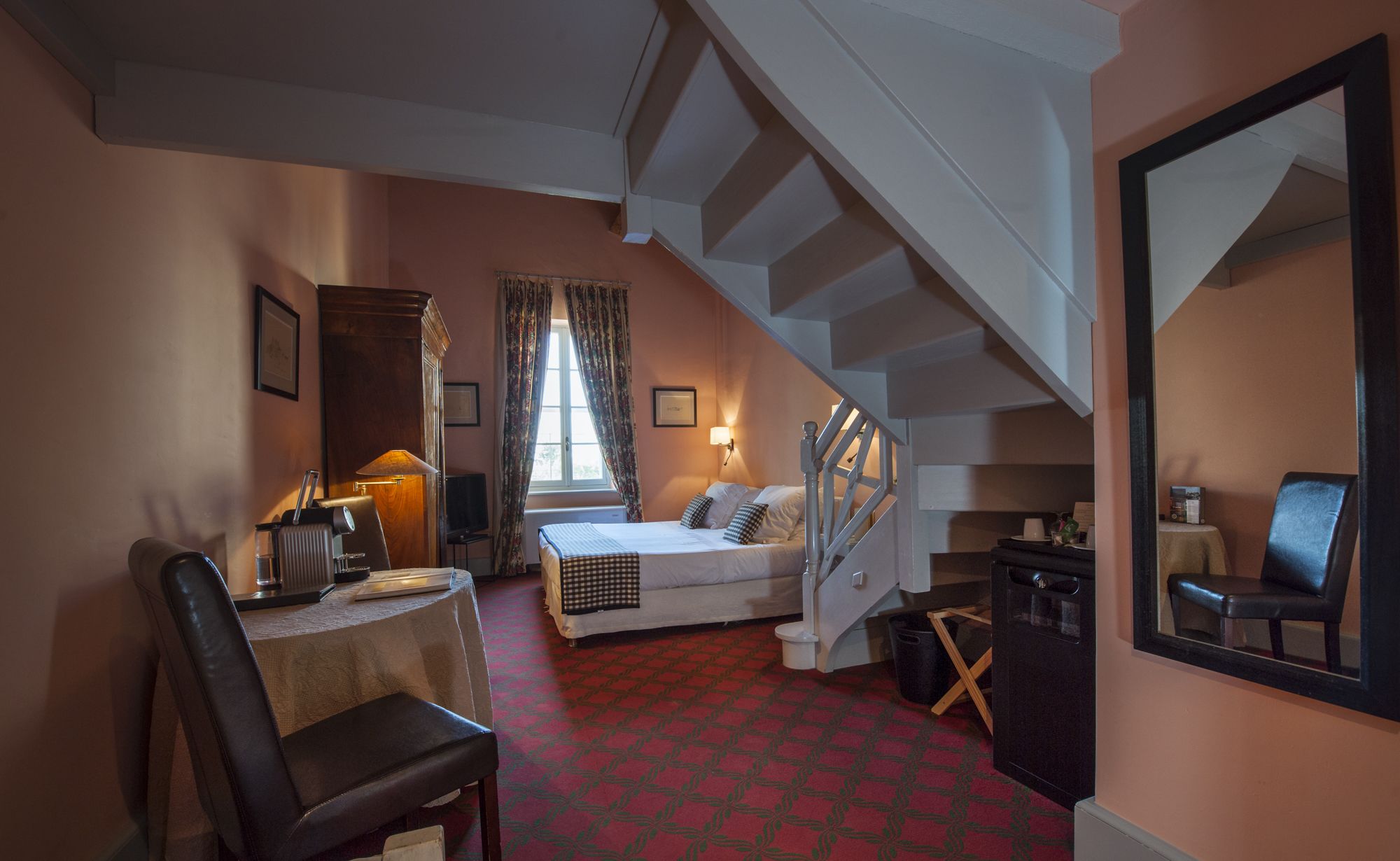 Una habitación de hotel con cama, escritorio, silla, espejo y una escalera.