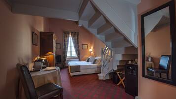 Una habitación de hotel con cama, escritorio, silla, espejo y una escalera.