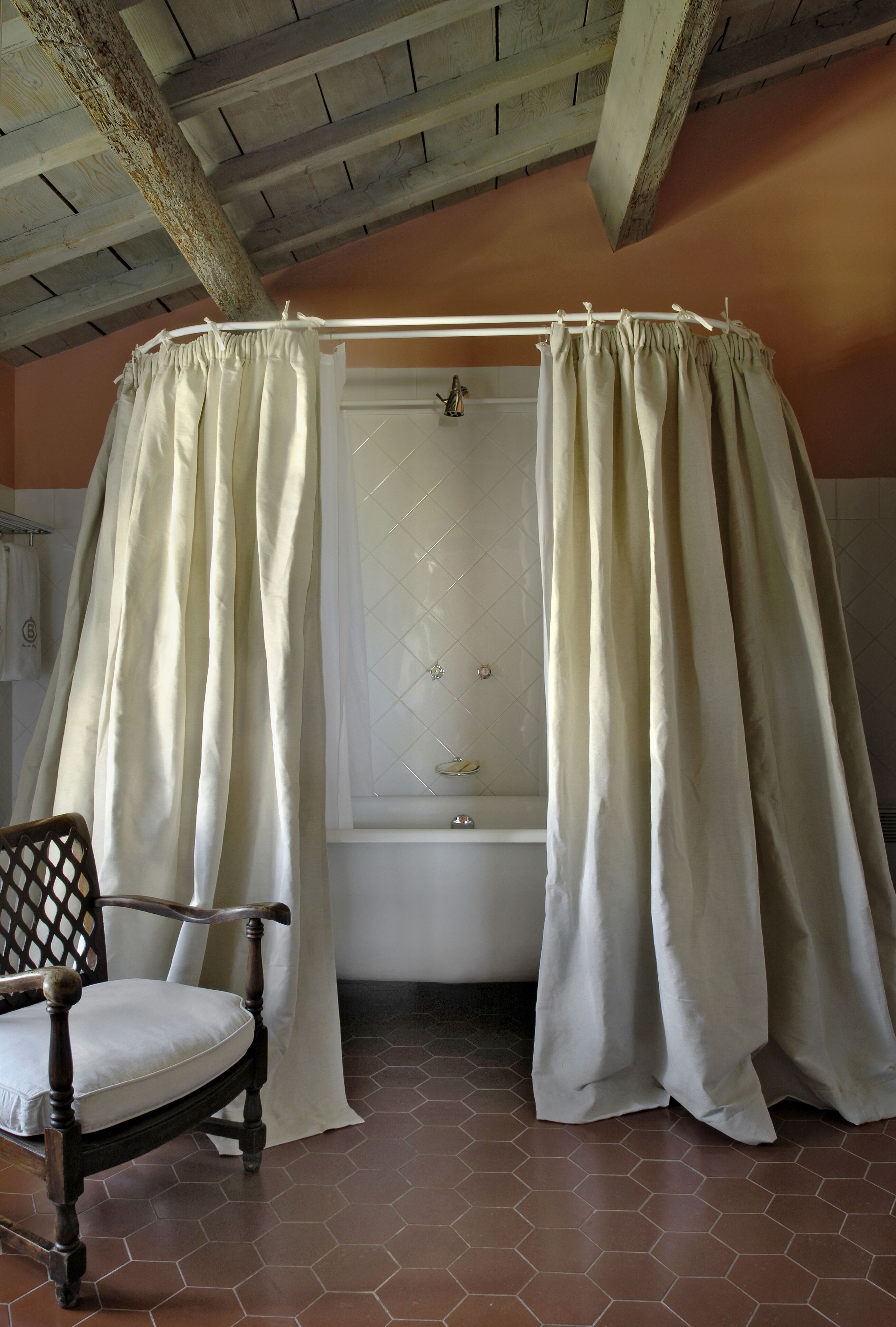 A bathroom with a bathtub, a wooden chair, and a window with a curtain.