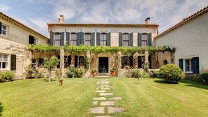 A courtyard with a stone pathway leading to a building with a traditional facade, stone pillars, and a covered entrance. - Le Mas De Peint (Arles)