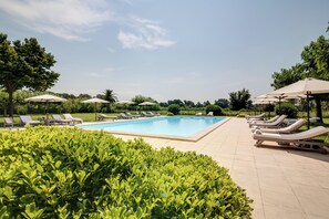 Una piscina con tumbonas y sombrillas, rodeada de vegetación cuidada.