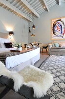 Una habitación de hotel moderna con una cama grande, una mesa de comedor, un sofá y un cuadro abstracto de gran tamaño en la pared.