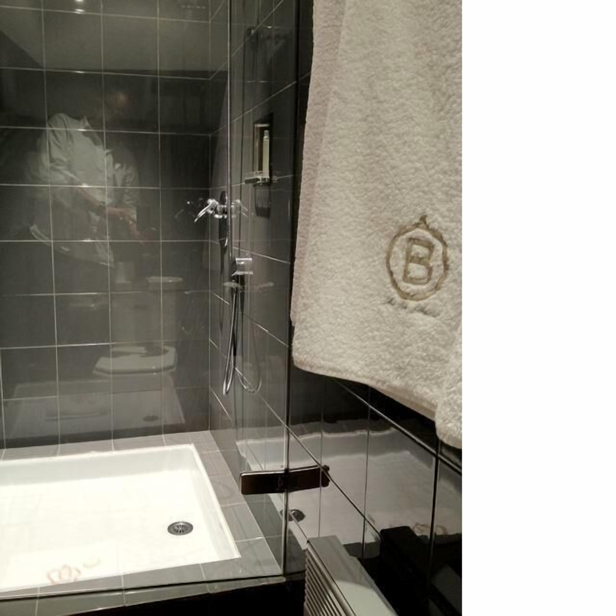 A modern bathroom with a glass-enclosed shower, a white bathtub, and a towel with a monogram.