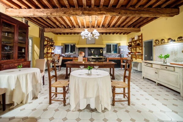 Comedor con mesa redonda y sillas, techo de madera y cocina al fondo.