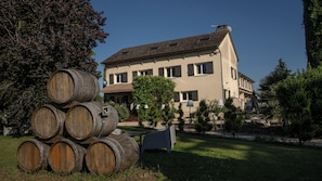 A large building with a tiled roof, multiple windows, and a sign indicating it is a hotel. There are wooden barrels stacked in the foreground, and a well-maintained lawn with a few trees and a lamp post. - Hôtel Parc Adélie (Montagny-les-Beaune)