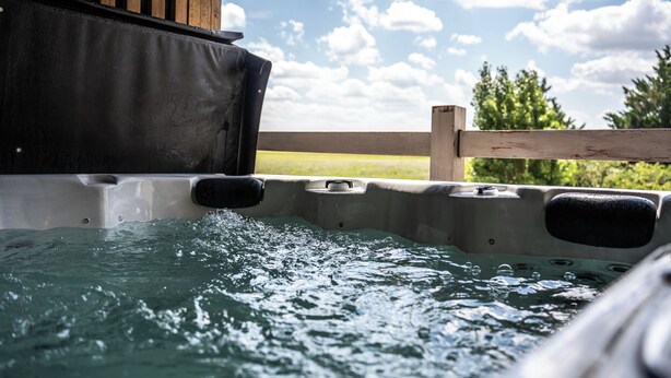 A hot tub with water flowing out, surrounded by a wooden fence and greenery. - Hôtel Parc Adélie (Montagny-les-Beaune)