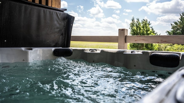 A hot tub with water flowing out, surrounded by a wooden fence and greenery. - Hôtel Parc Adélie (Montagny-les-Beaune)