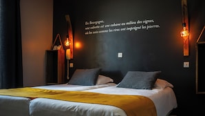 A modern hotel room with a large bed, two pillows, a yellow throw blanket, and a wall with a French quote. - Hôtel Parc Adélie (Montagny-les-Beaune)