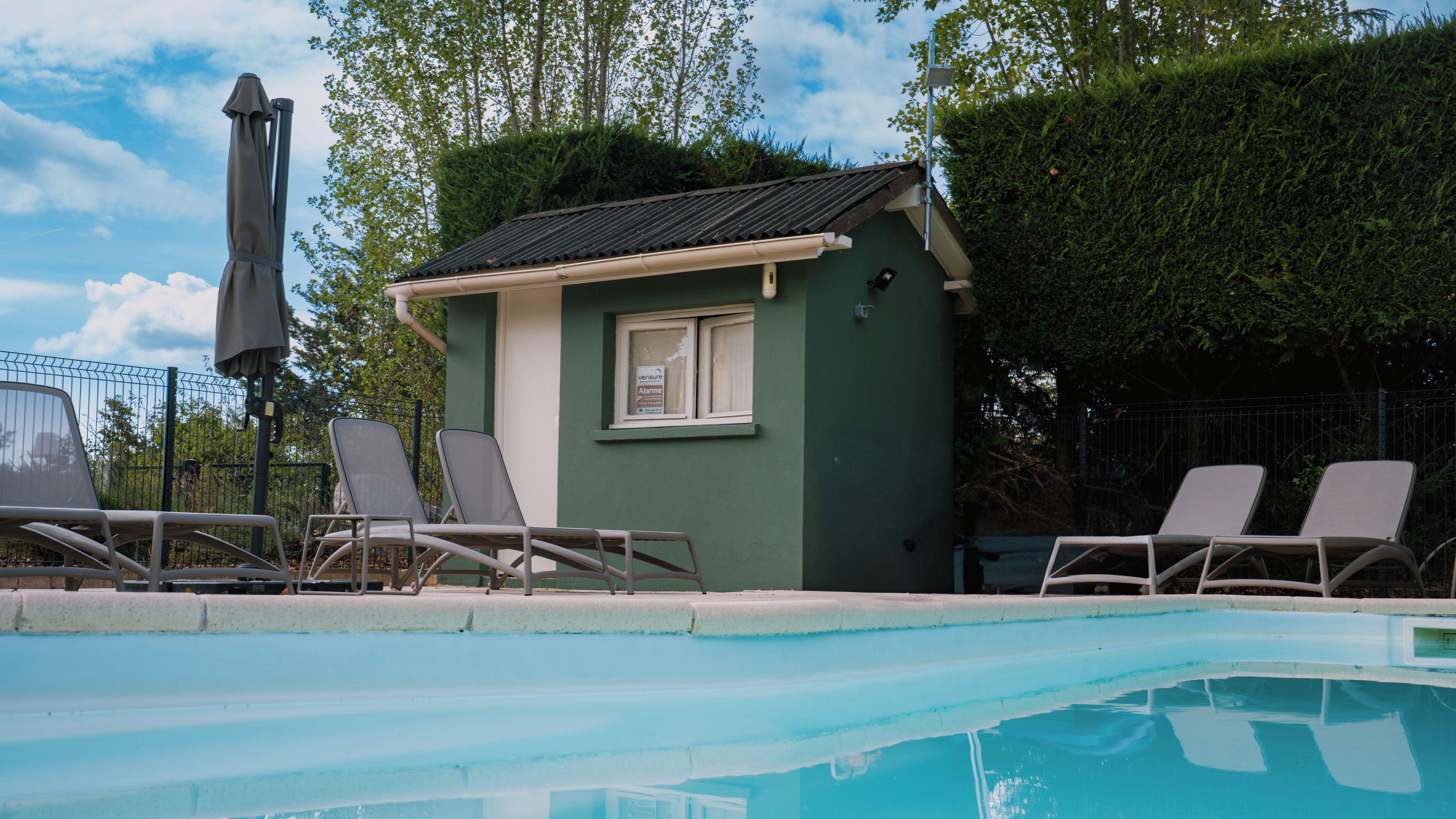 A small building with a window, adjacent to a swimming pool with lounge chairs.
