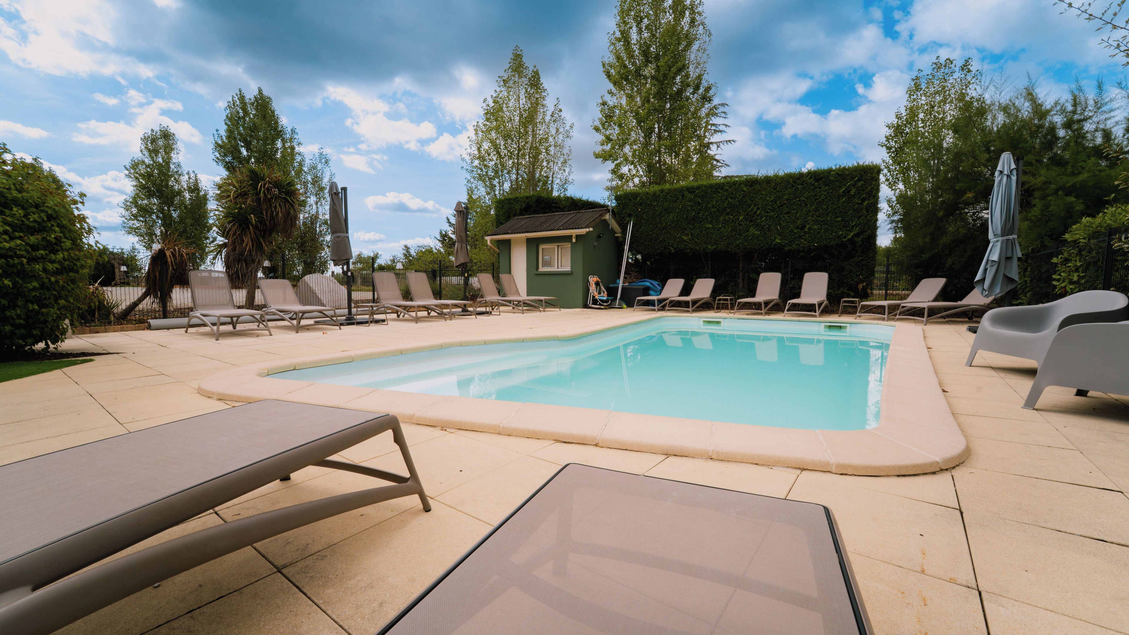 Una piscina con sillones de descanso y un edificio pequeño al fondo.