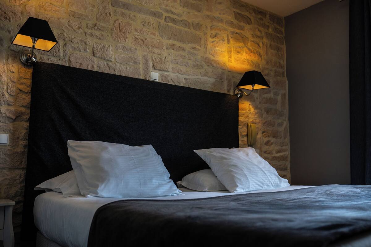 A bed with white linens, a dark headboard, and two wall-mounted lamps.