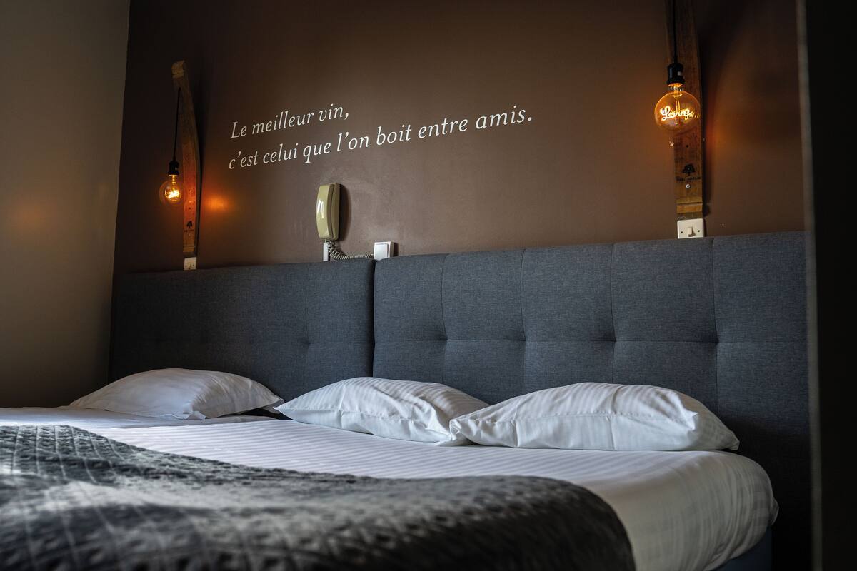 A hotel room with a large bed, a headboard, and a wall with a quote in French.
