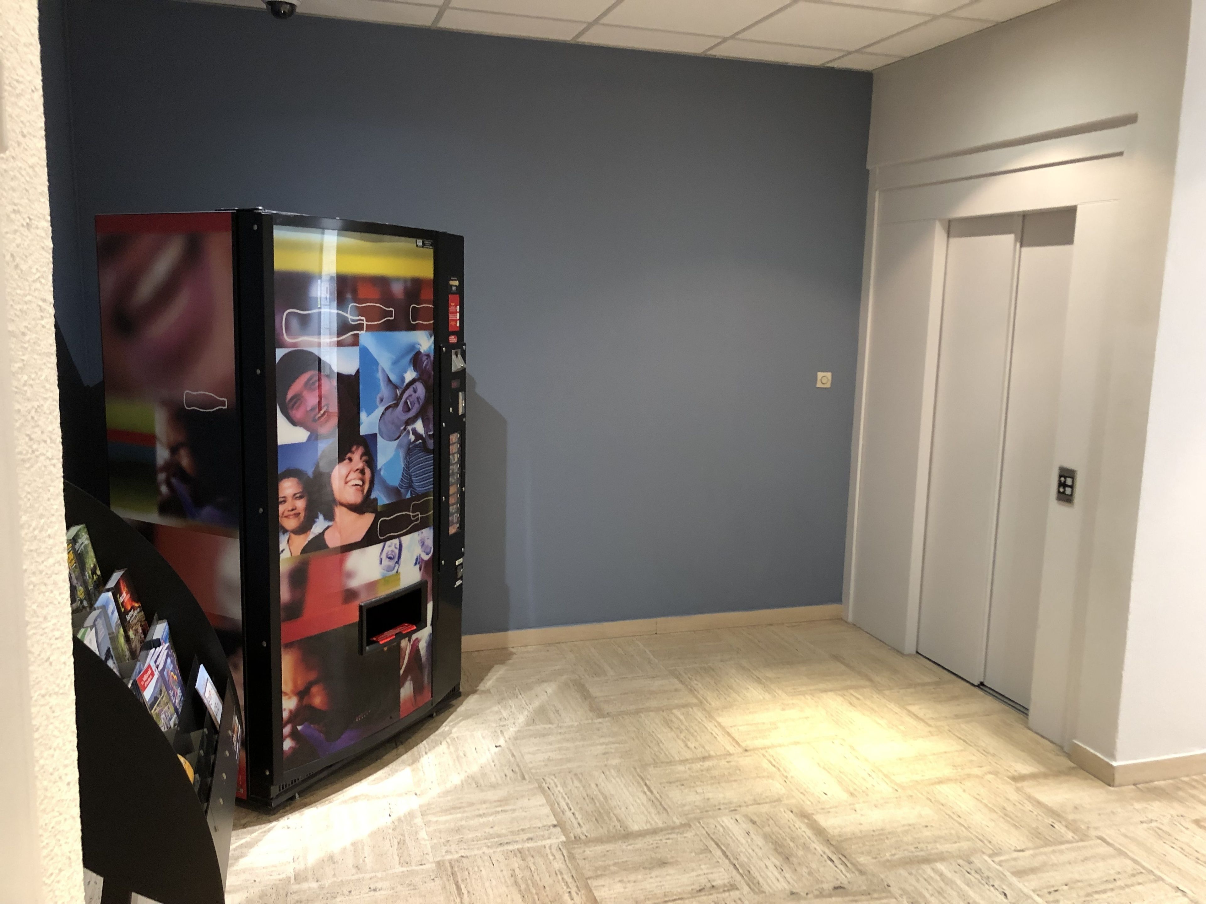 Un couloir avec un distributeur automatique affichant des photos, une porte et un interrupteur sur le mur.