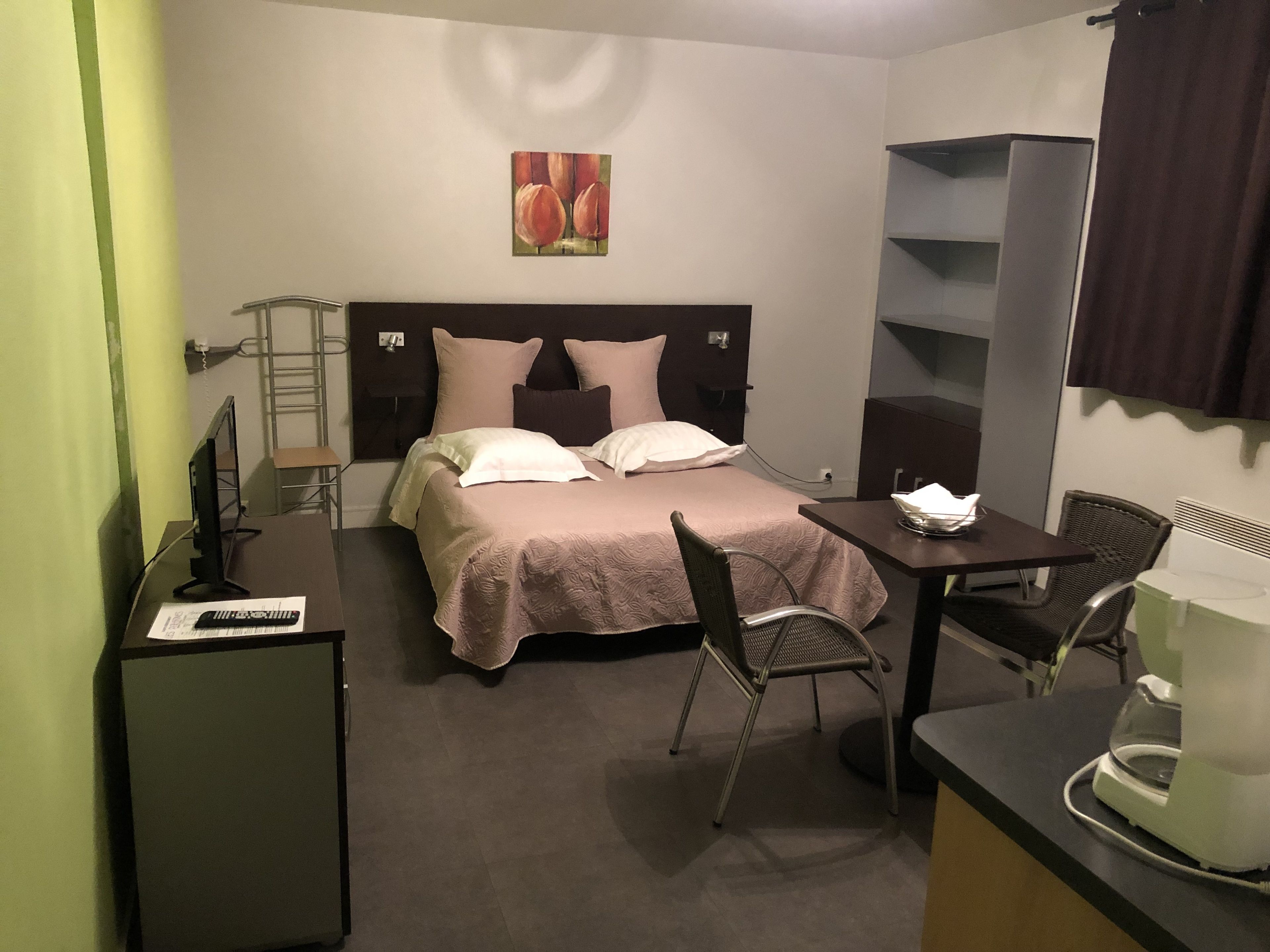 Hotellihuone, jossa on sänky, työpöytä, tuoli, kahvinkeitin ja televisio.