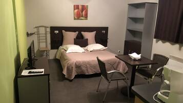 Hotellihuone, jossa on sänky, työpöytä, tuoli, kahvinkeitin ja televisio.