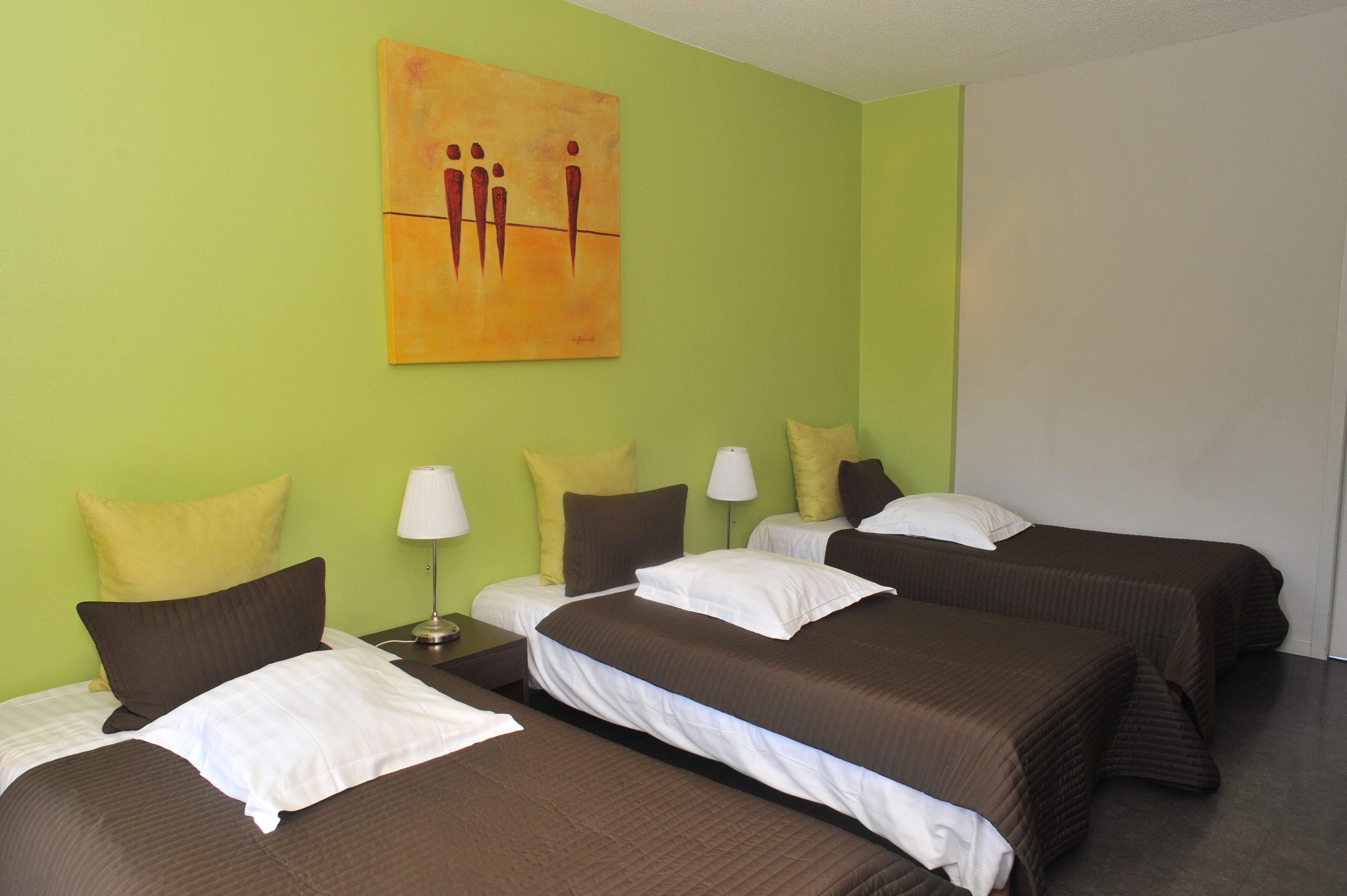 A hotel room with three beds, each with brown bedding and white pillows. There is a painting on the wall above the beds.