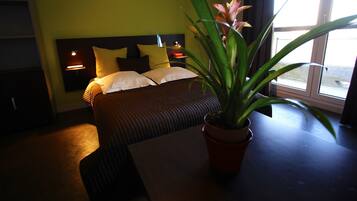 Una habitación de hotel con una cama, lámparas de noche, una planta en maceta y una ventana.