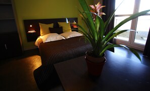 Et hotelværelse med en seng, sengeborde med lamper, en potteplante og et vindue.