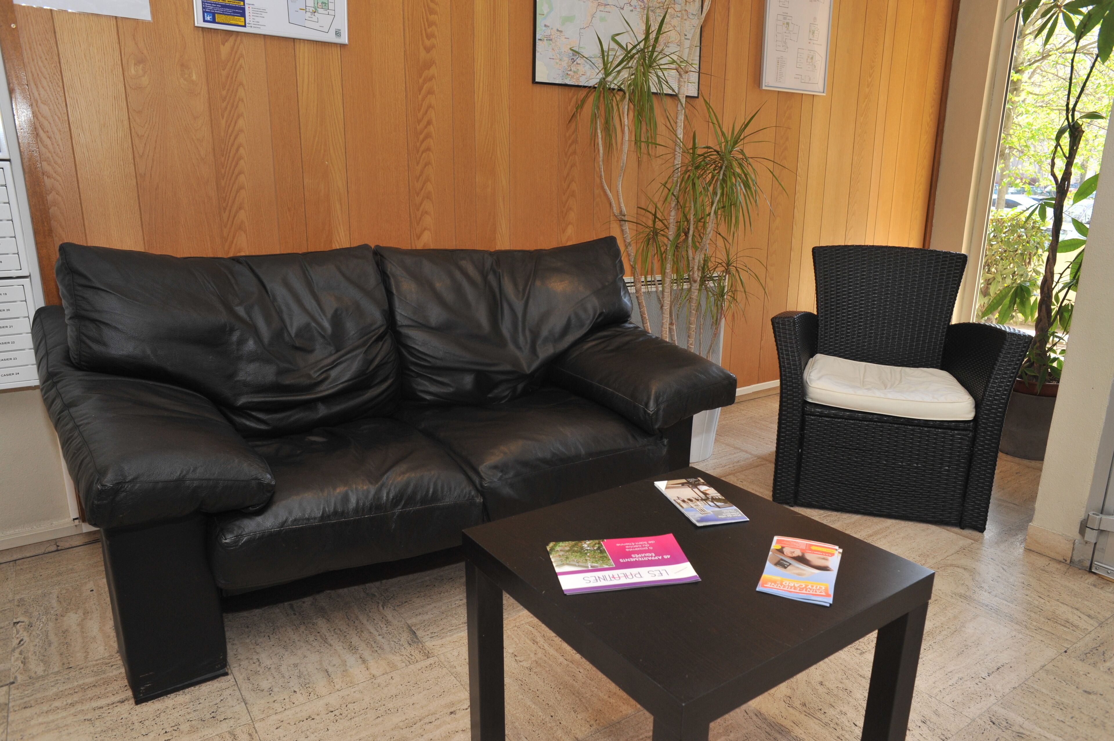 A black leather sofa and a wicker chair in a room with wooden walls, a tiled floor, and a potted plant.