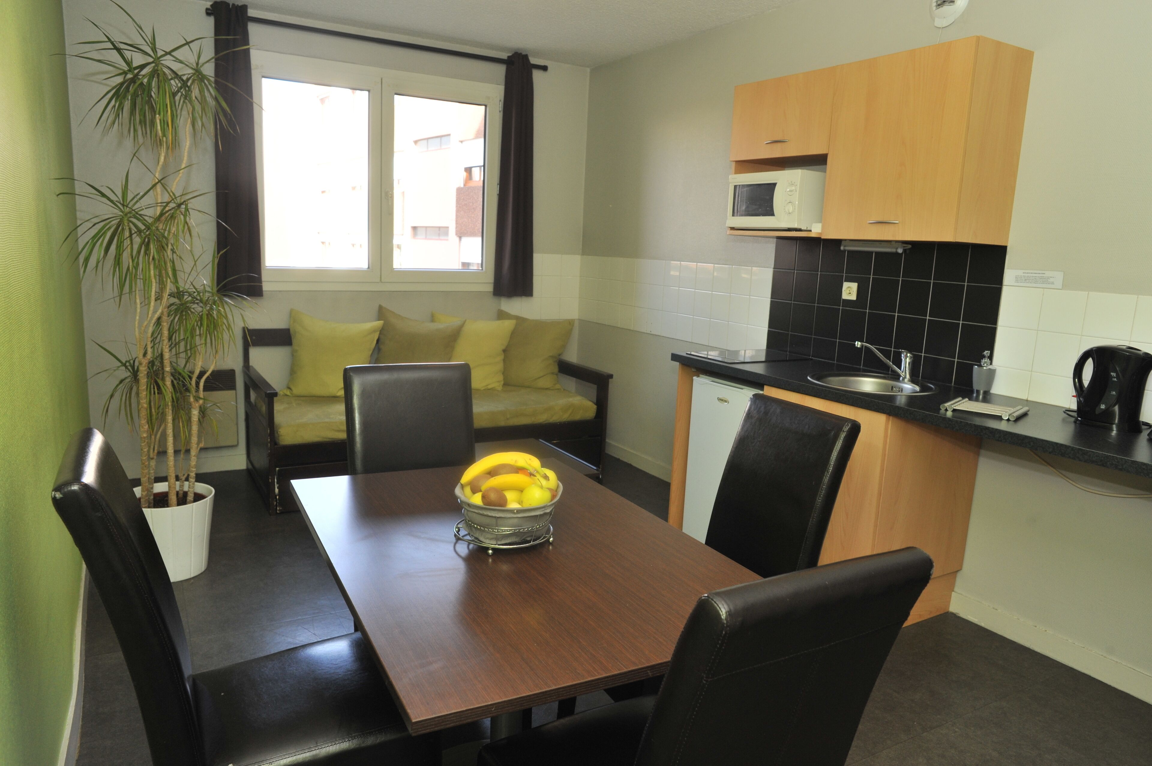 Una cocina compacta con una mesa, sillas, una planta en maceta y una ventana con cortinas.
