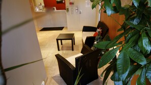 A hotel lobby with a reception desk, seating area, and a plant. - Les Palatines - Residence (Saint-Etienne)