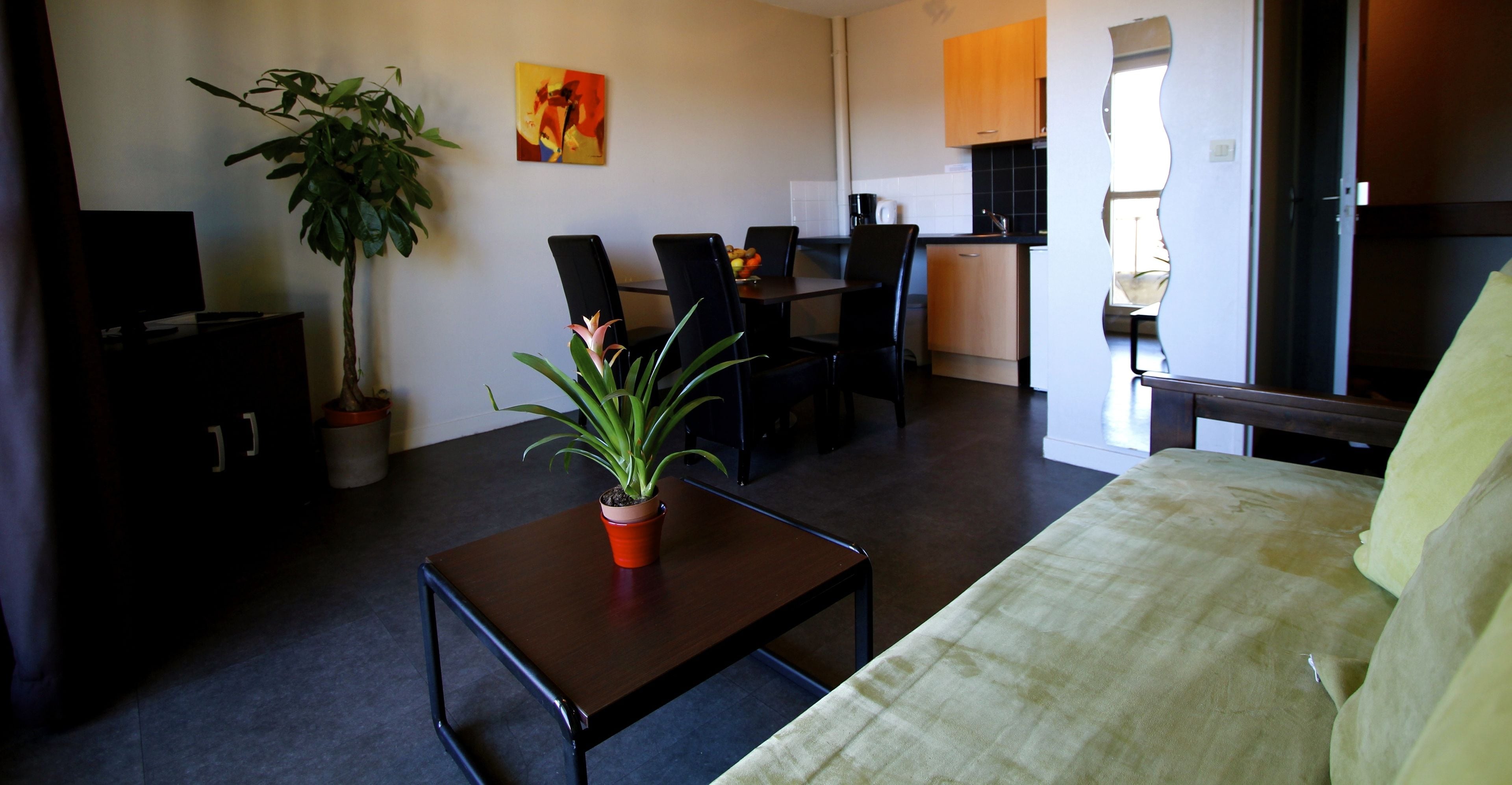 A living room with a sofa, a coffee table, a dining table with chairs, a potted plant, and a painting on the wall.