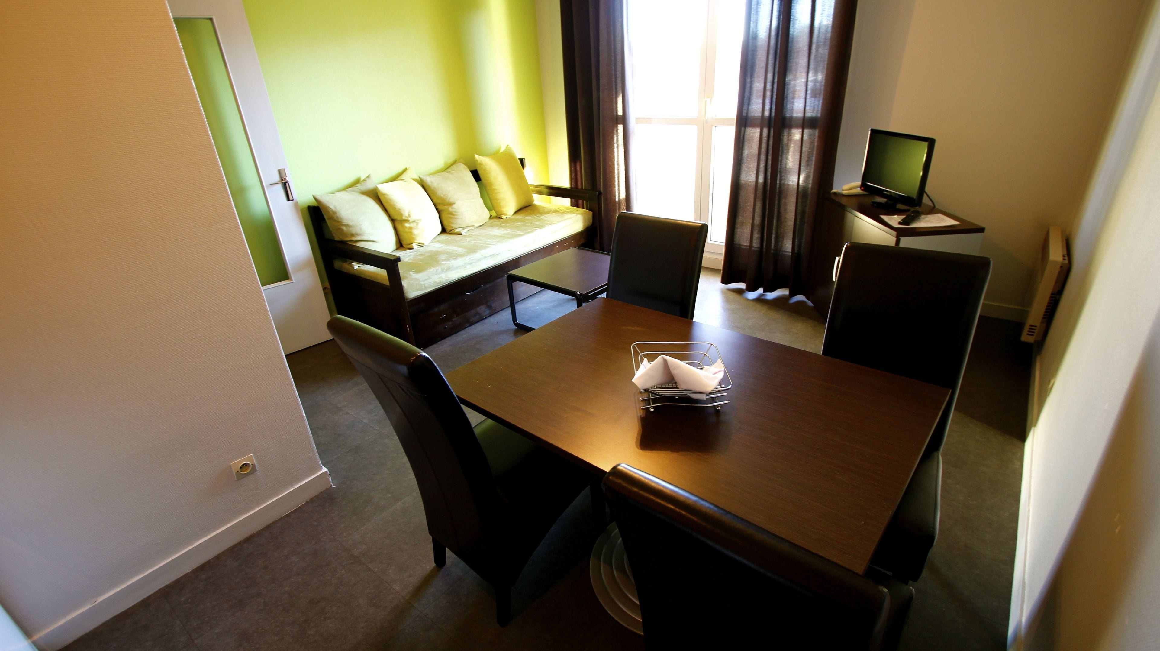 A compact room with a bed, a desk with a computer, and a dining table.
