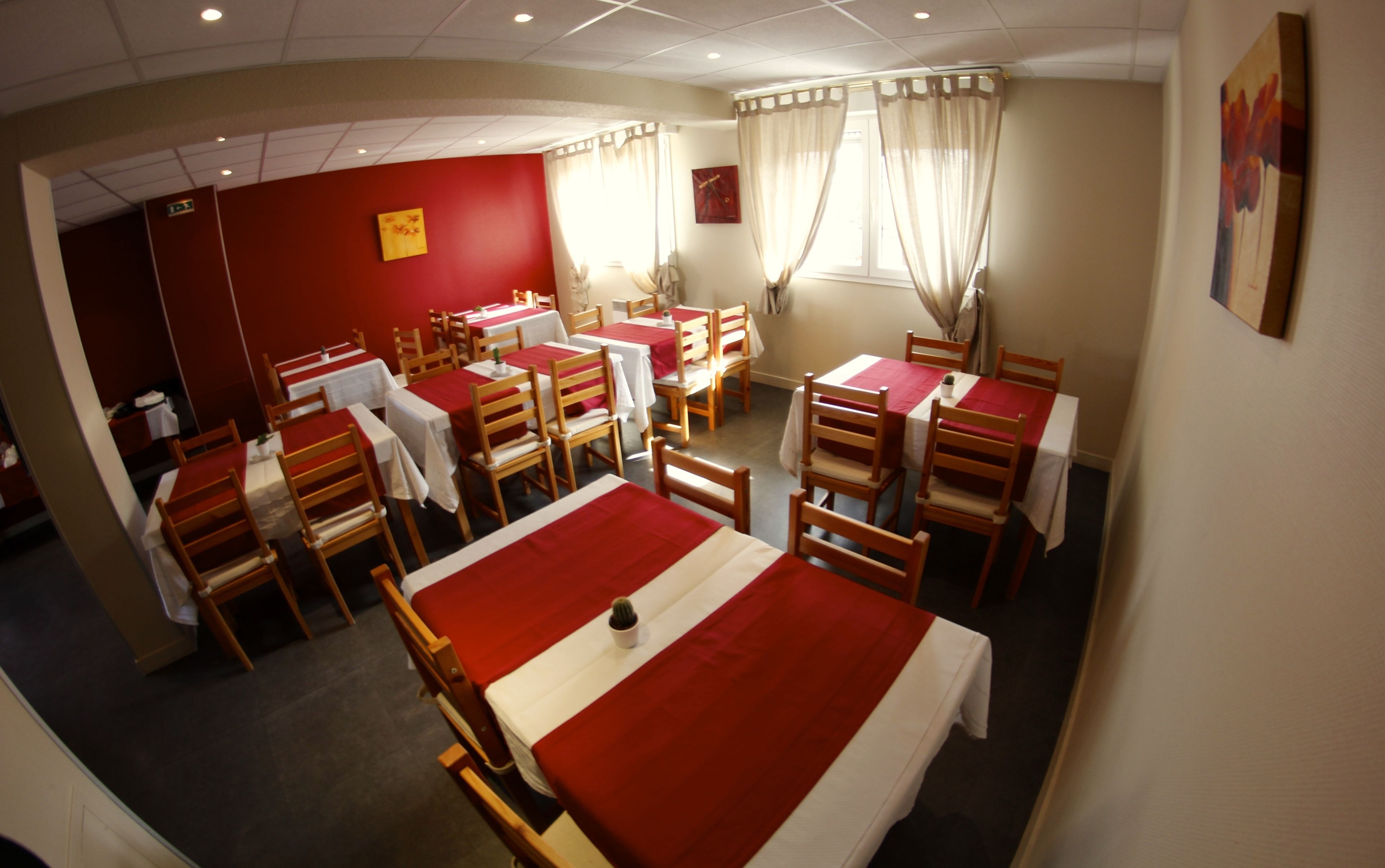 A restaurant with multiple tables and chairs, red tablecloths, and a red wall with a clock.
