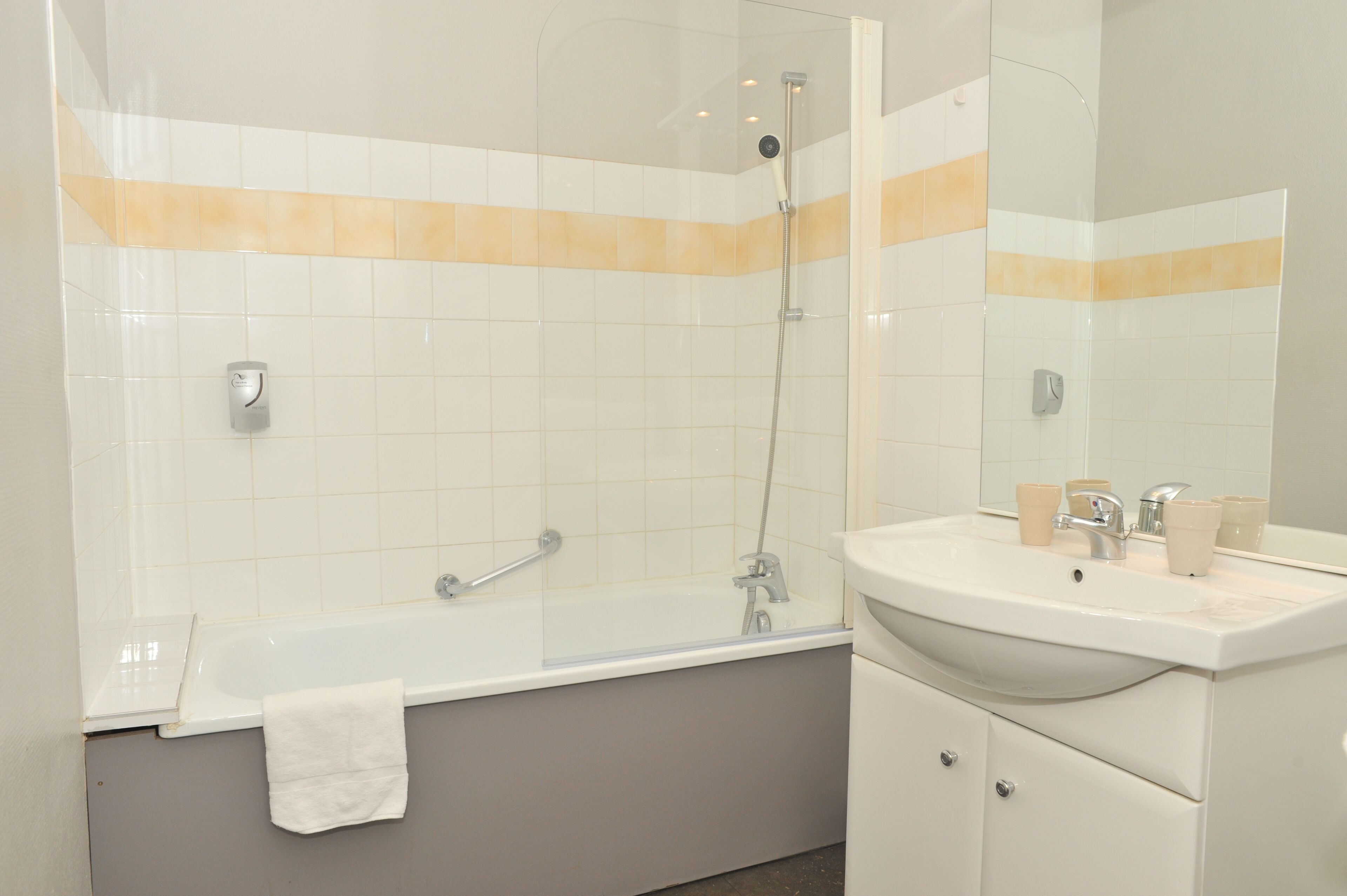 A modern bathroom with a glass-enclosed shower, a white sink with a mirror, and a towel hanging on the tub.
