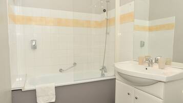 Un bagno moderno con doccia vetrata, un lavandino bianco con specchio e un asciugamano appeso alla vasca.