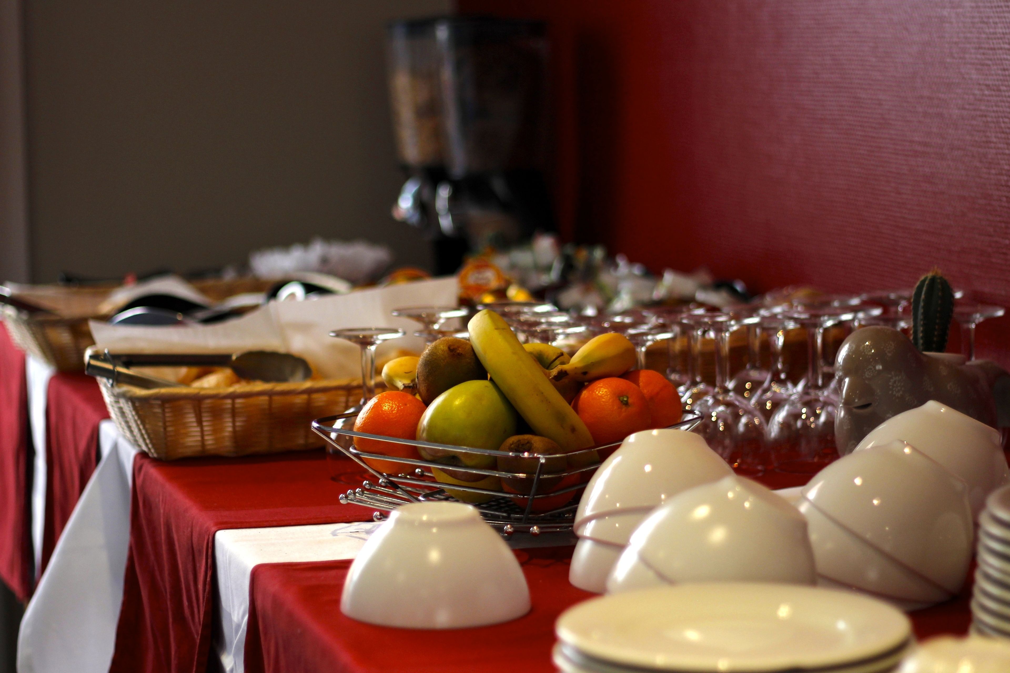 Una mesa de buffet con una variedad de frutas, como plátanos, manzanas y naranjas, y una máquina de café al fondo.