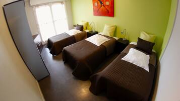 A hotel room with three single beds, a refrigerator, a window with curtains, and a painting on the wall.