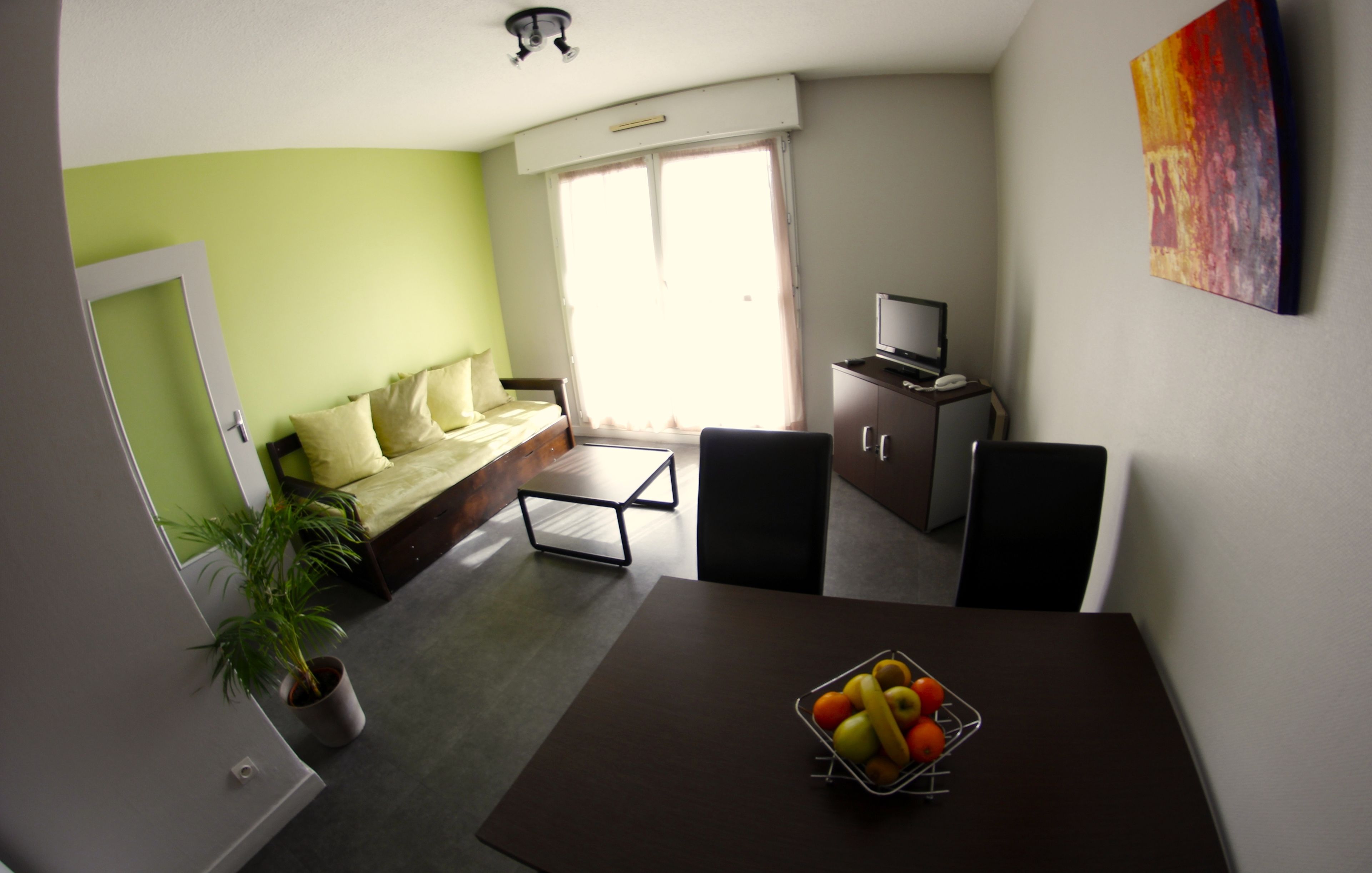 Un espacio habitable pequeño con una cama, una mesa de comedor con fruta, un televisor y una planta.