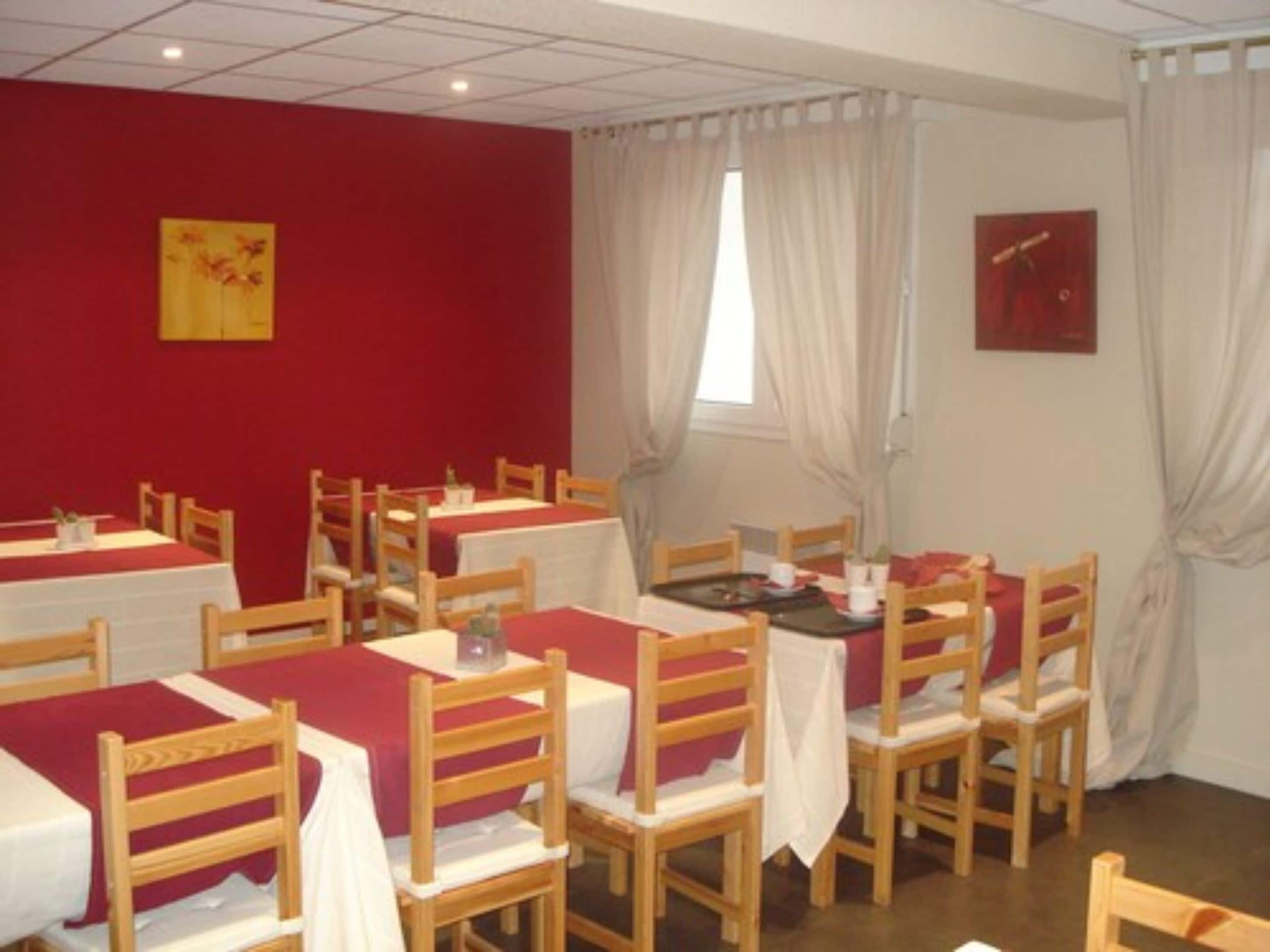 Un comedor con mesas y sillas, paredes rojas y dos cuadros.