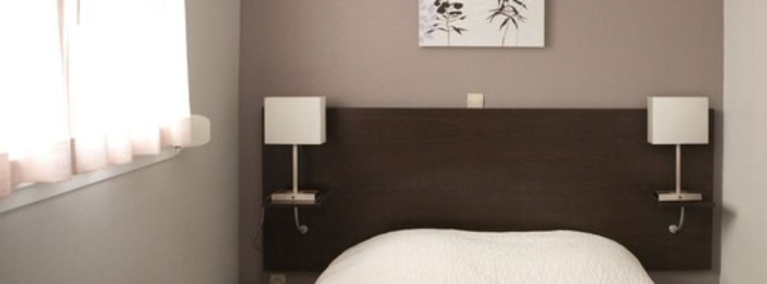 A bedroom with a dark headboard, two bedside lamps, and a framed artwork on the wall.