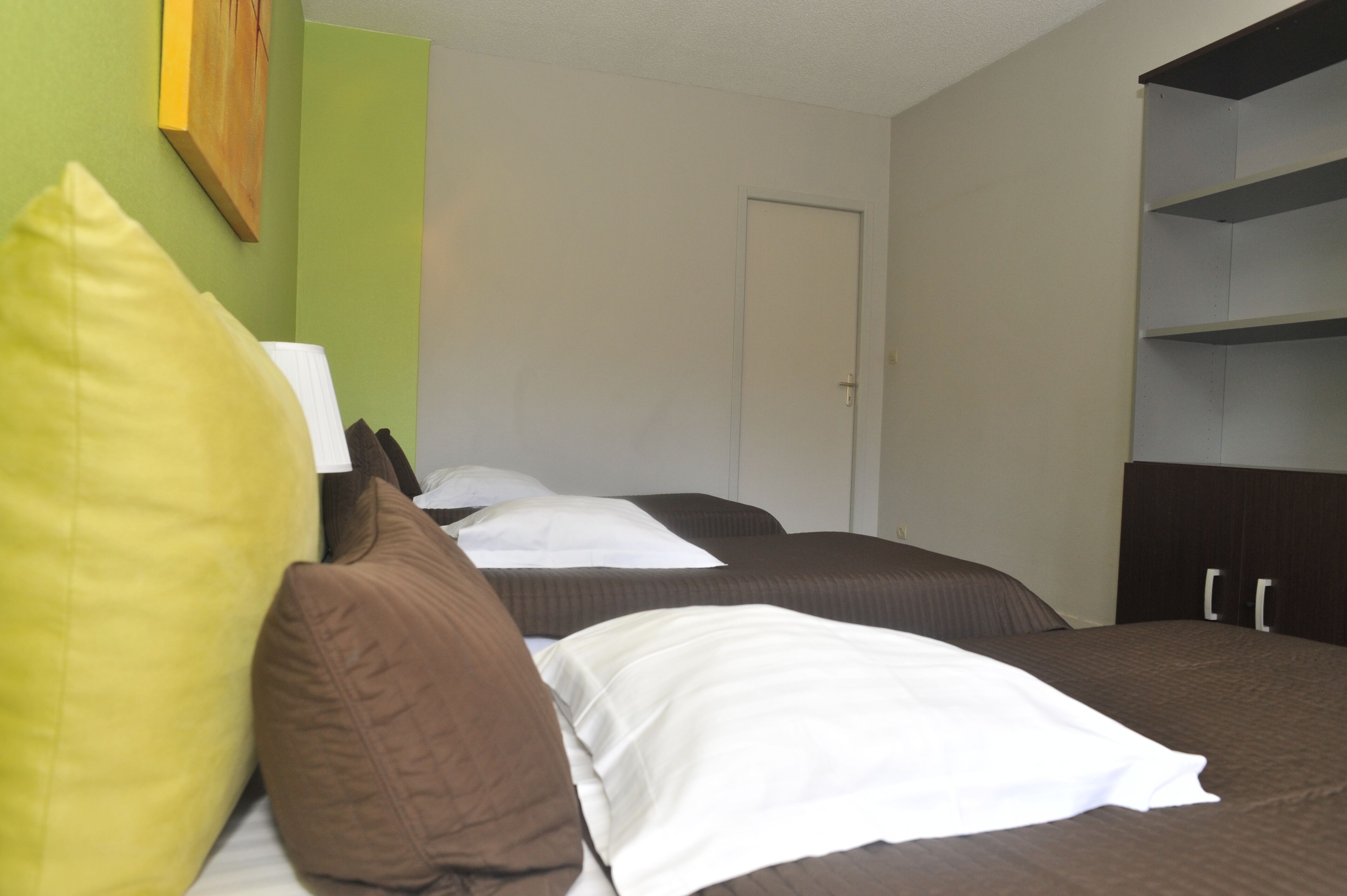Quarto de hotel com duas camas, uma porta e uma estante.