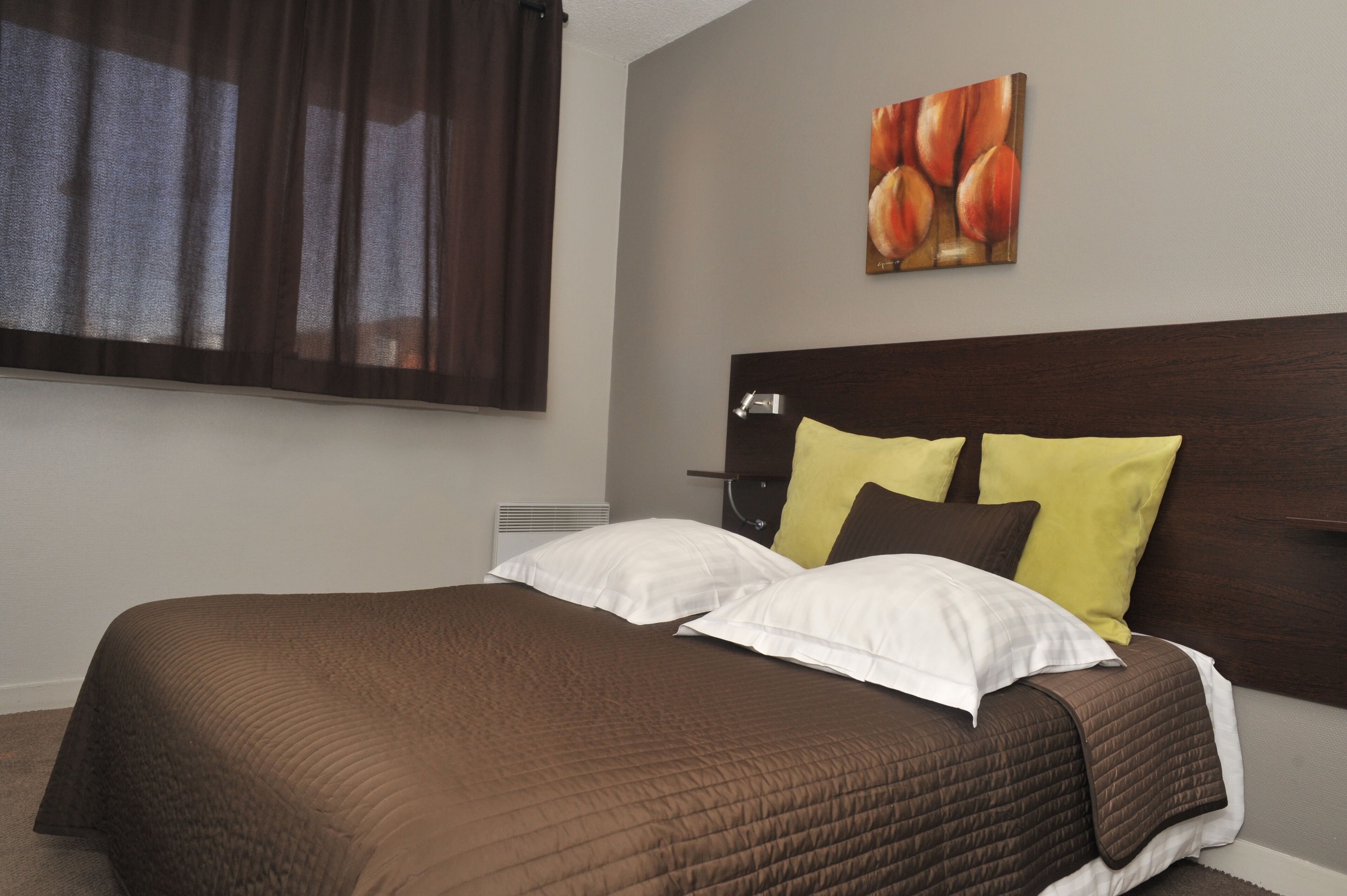 Een net opgemaakt bed met een bruine quilt, witte en gele kussens en een donker hoofdbord.