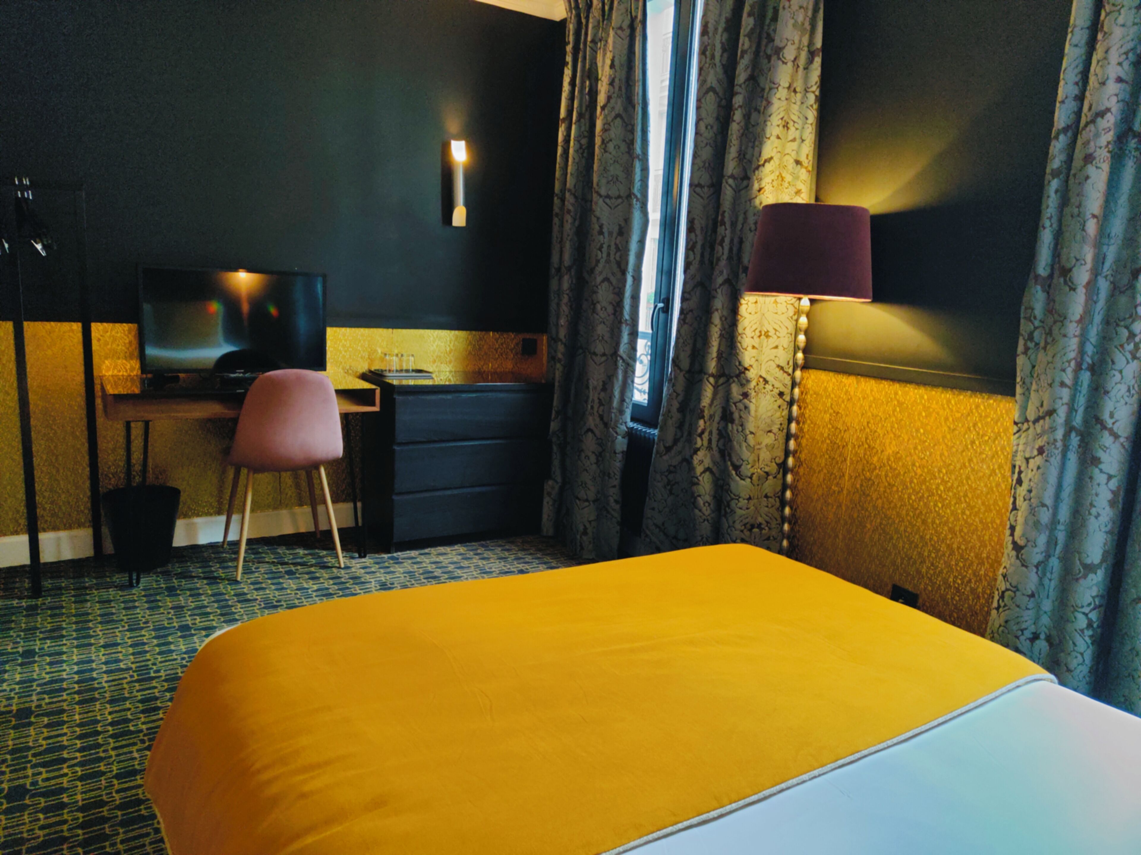 A hotel room with a large bed, a desk with a chair, a television, and a window with curtains.