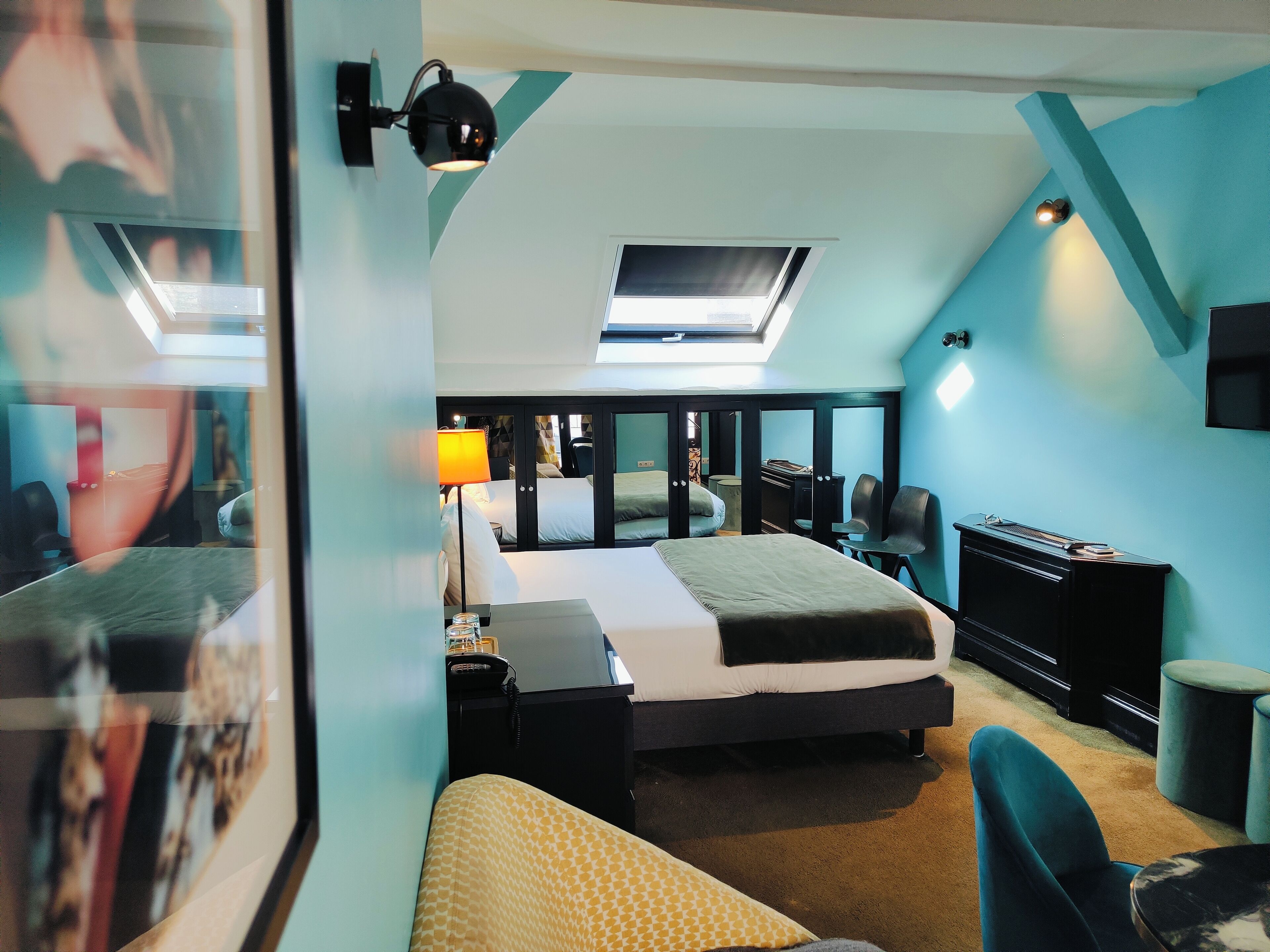 A modern hotel room with a skylight, a bed, a desk, and a seating area.
