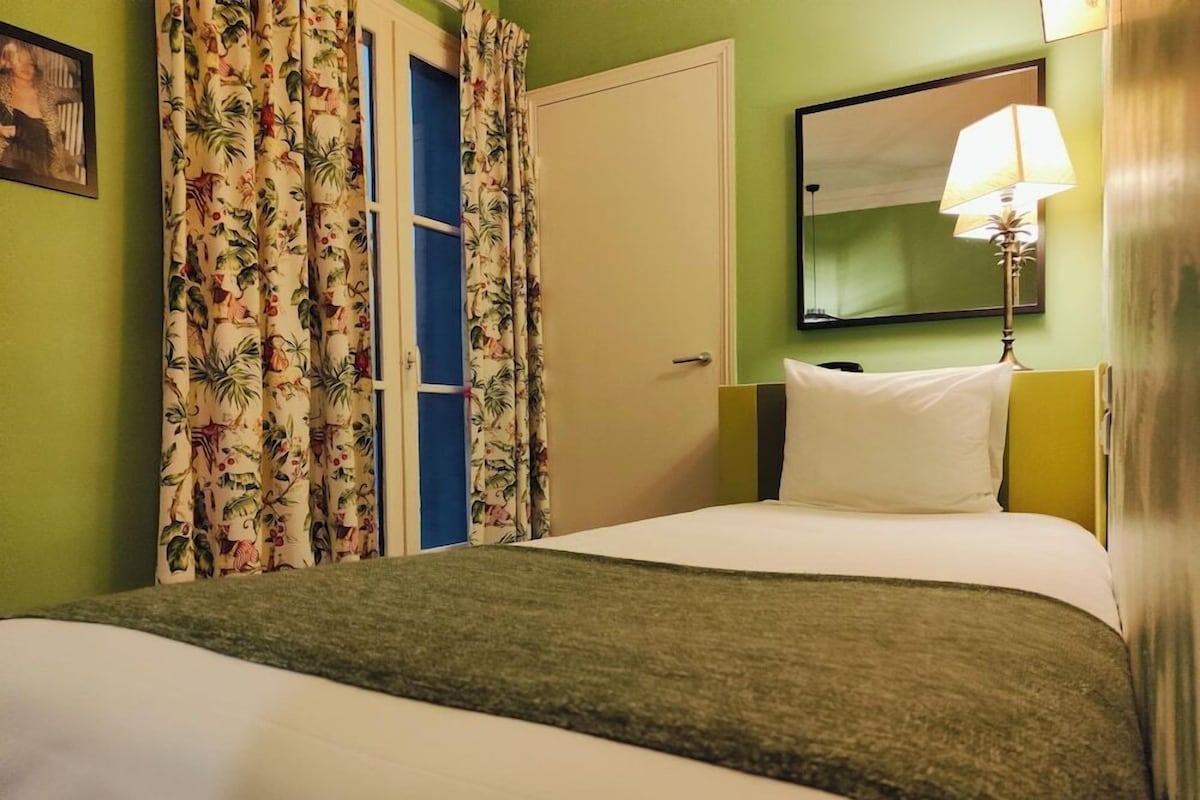 Habitación de hotel con cama, mesita de noche, lámpara, espejo y puerta con cortinas.