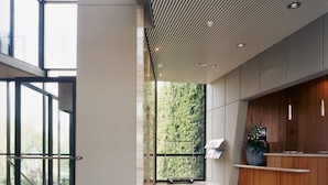 A spacious lobby with a high ceiling, a reception desk, and a view of greenery outside.