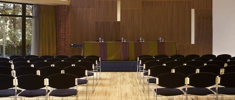 A conference room with rows of chairs, a stage with a table, and a brick wall.