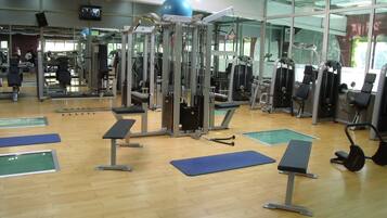 Un gimnasio con diversos equipos de ejercicio, suelo de madera y espejos.