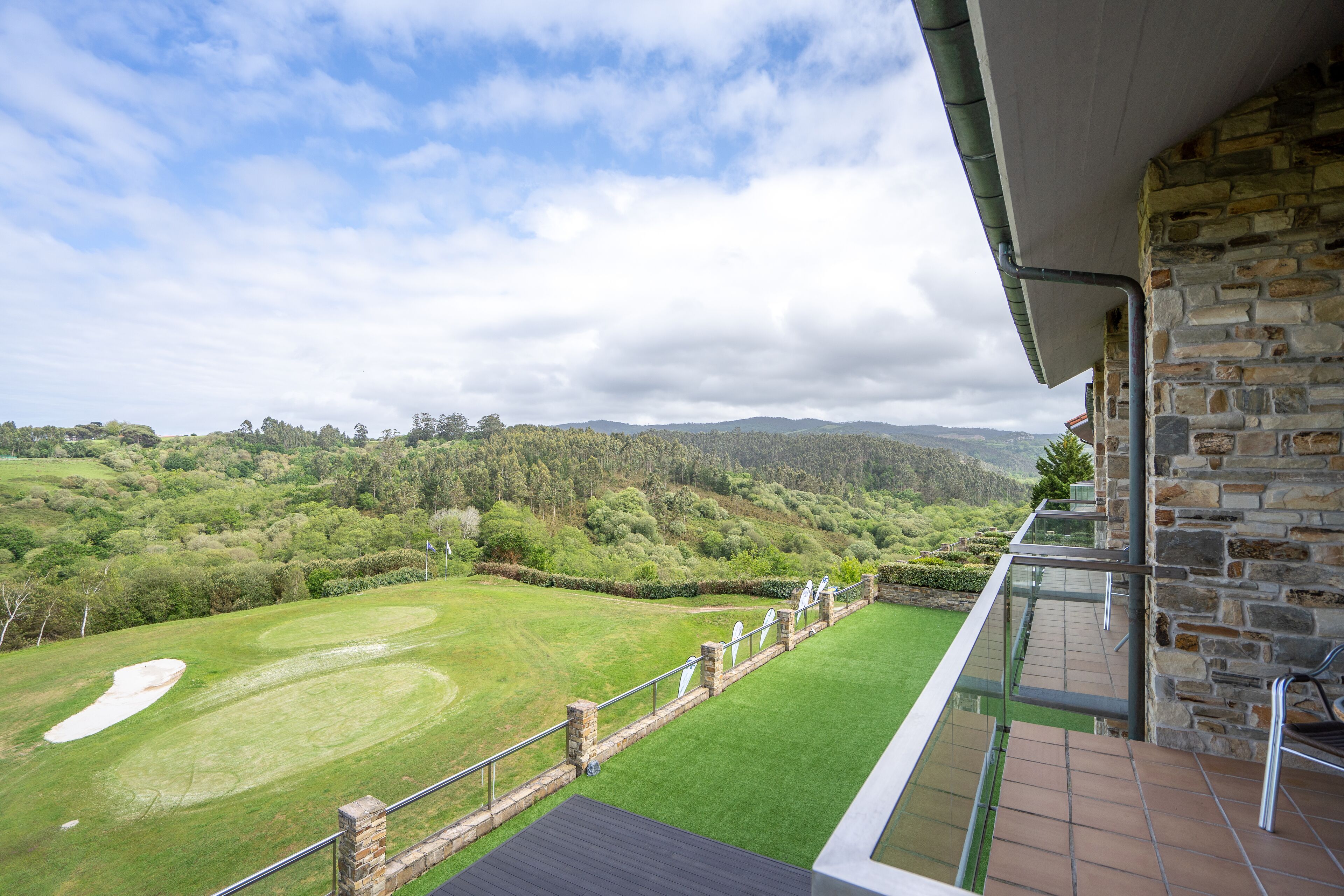 A view from a balcony overlooking a golf course with a stone wall and glass railing.
