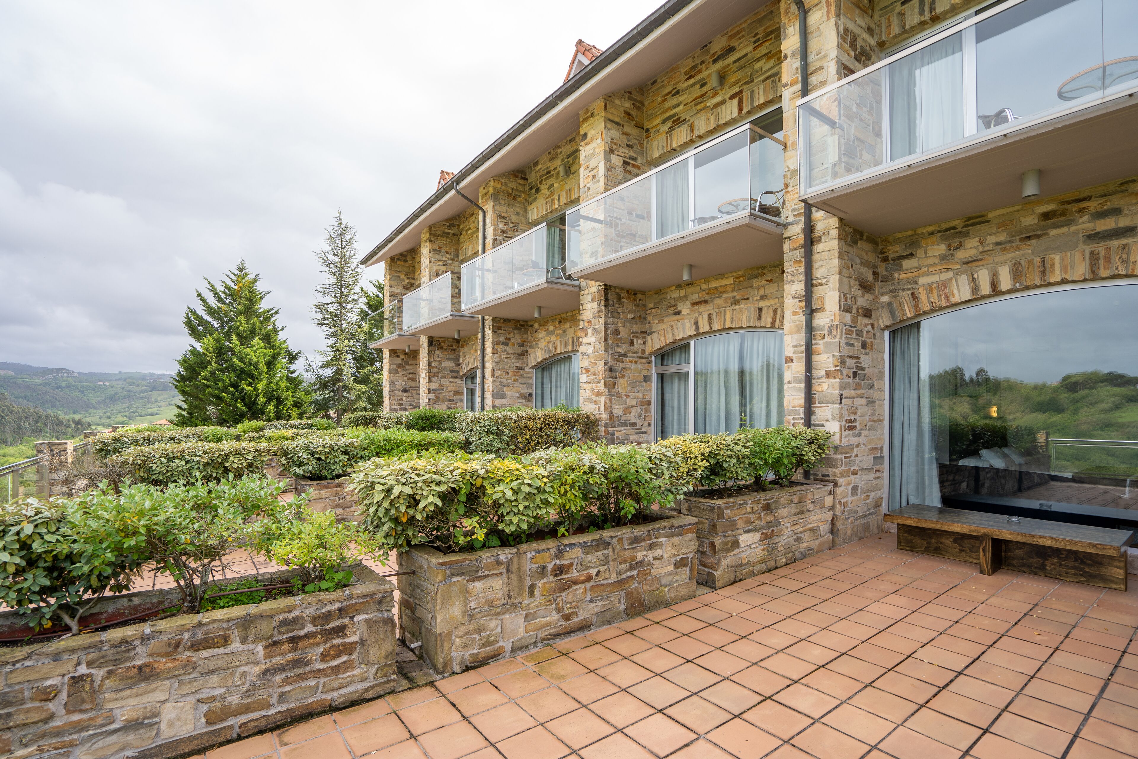 A multi-story stone building with balconies, large windows, and a terraced garden area.