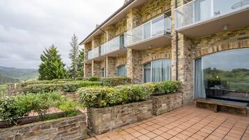 A multi-story stone building with balconies, large windows, and a terraced garden area.