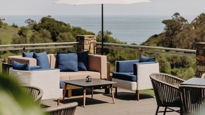 Una terraza con un conjunto de sofás, una mesa y sillas, con vistas a un paisaje marino y vegetación.