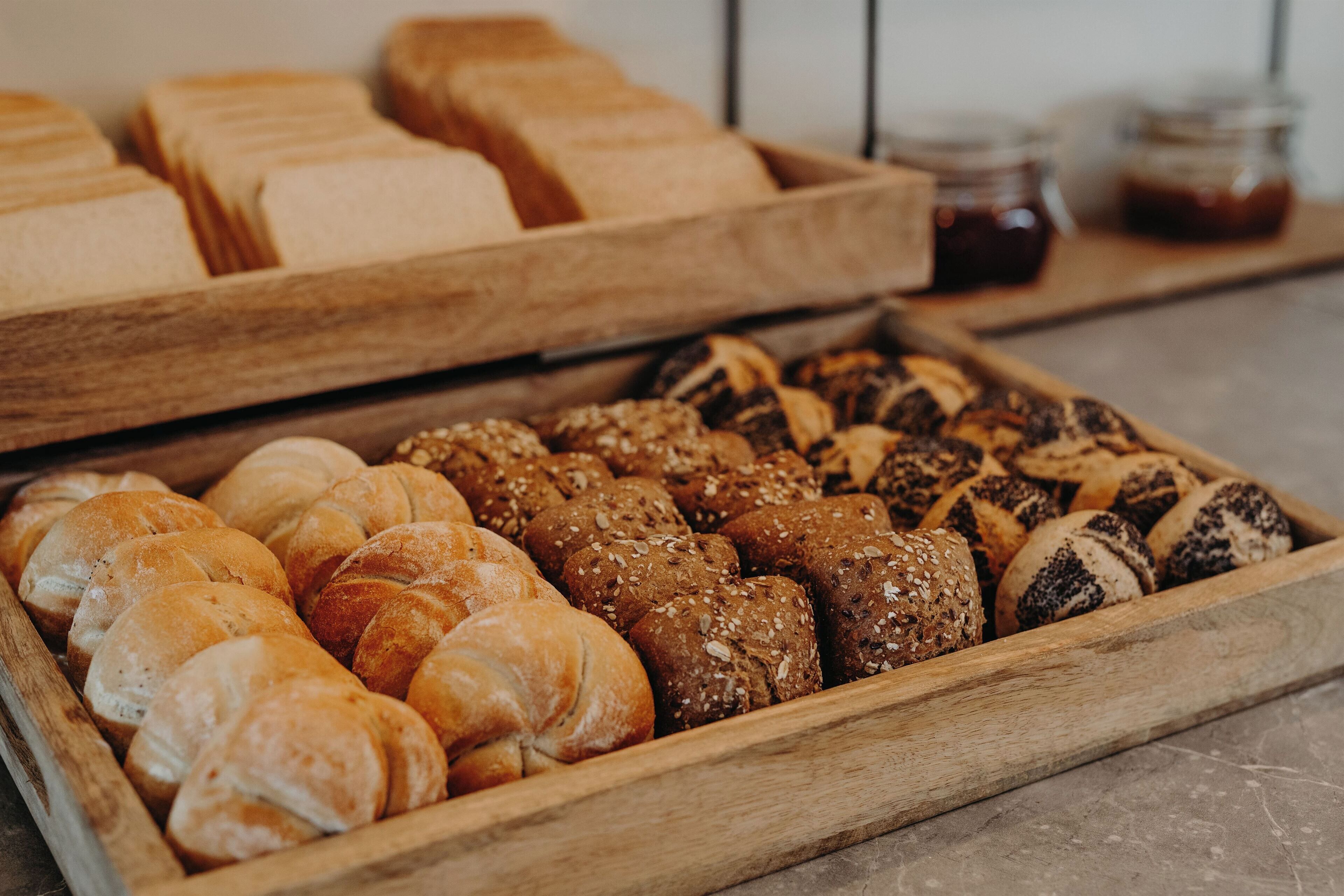 A wooden tray filled with various types of bread, including croissants and seeded rolls.