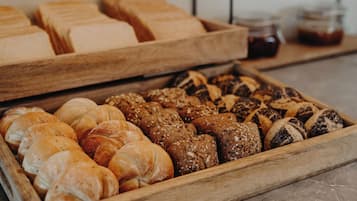 A wooden tray filled with various types of bread, including croissants and seeded rolls.